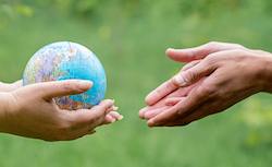 image of one pair of hands passing a globe to another pair of hands